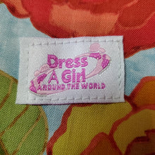 Load image into Gallery viewer, Fabric label with 'Dress a Girl Around the World' text on a colorful floral background